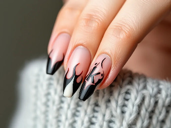 almond shaped acrylic nails with a nude base and black french tip flames with the letter k on the middle finger